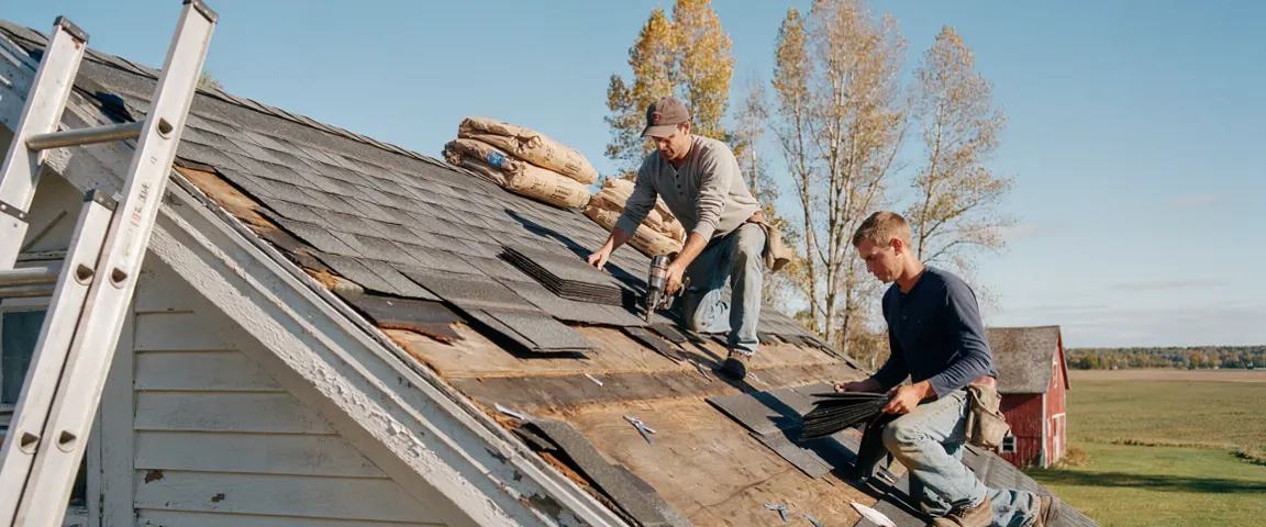 Two roofers laying new shingles on a farmhouse roof